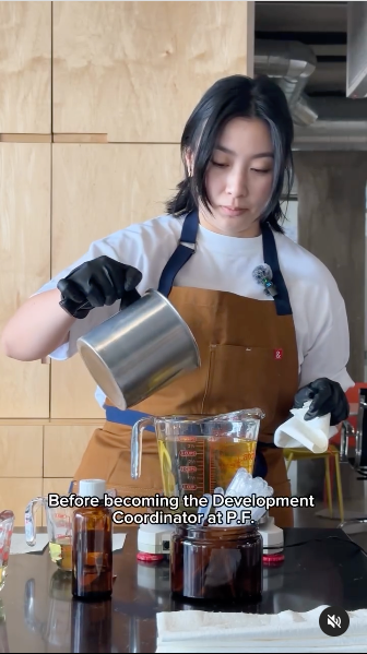 A woman in an apron is skillfully making a Candle liquid, surrounded by tools and ingredients on the counter.